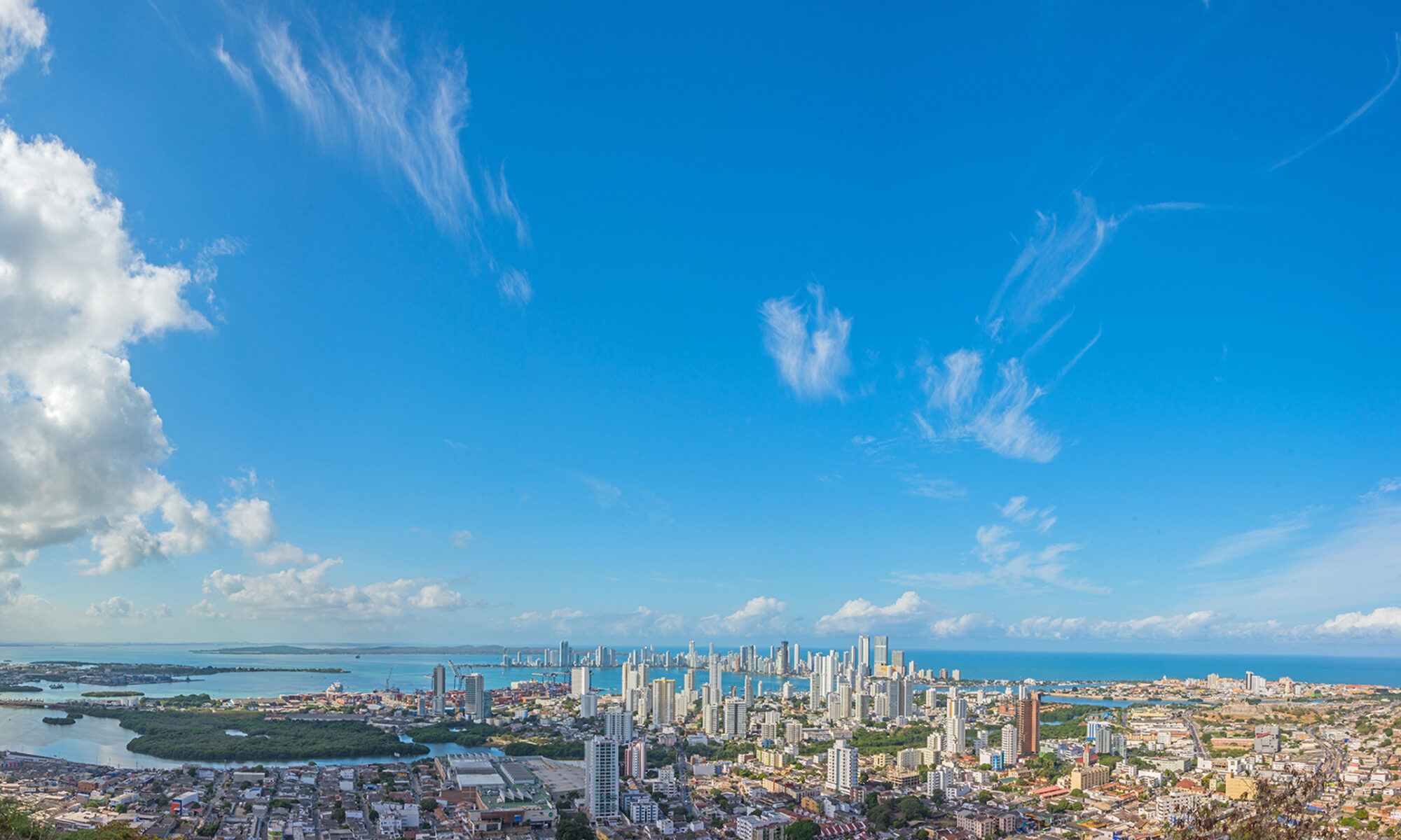 Panoramic view of Cartagena de Indias, showing the Bay, Bocagrande, the Historic Center and the island of Tierra Bomba under a deep blue sky that contrasts with the Caribbean Sea.